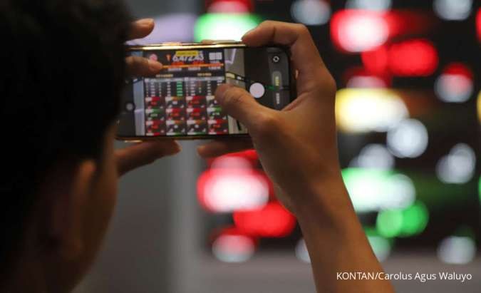 Investor memantau pergerakan IHSG dan harga saham melalui aplikasi papan kuotasi di depan layar bursa